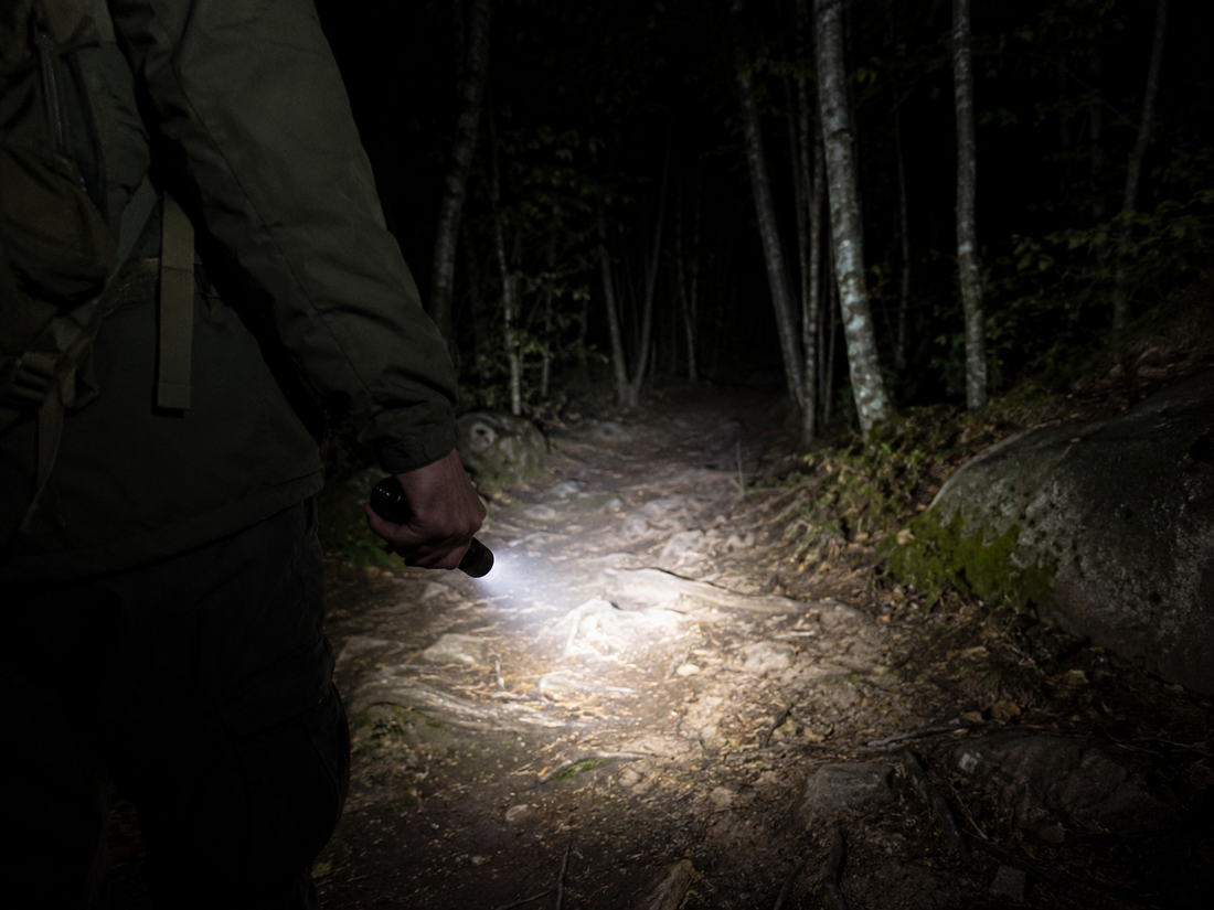 Person using a 300-lumen tactical flashlight to illuminate a dark wooded trail at night