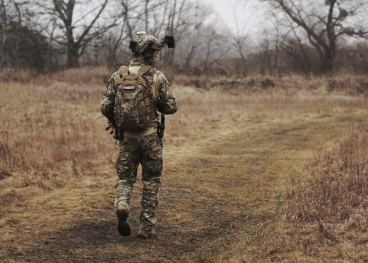 Tactical operator wearing helmet-mounted accessories during outdoor field movement.