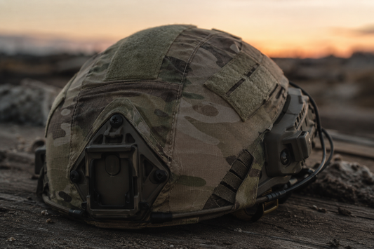 Tactical operator helmet with camouflage cover on rugged outdoor field surface.
